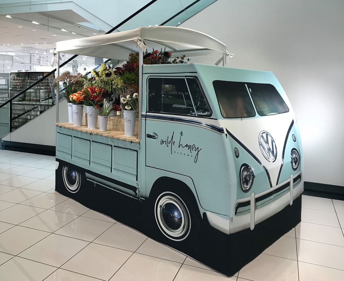 Life-size VW bus display for Wild Honey Blooms, styled as a flower cart with floral arrangements, displayed in a retail interior