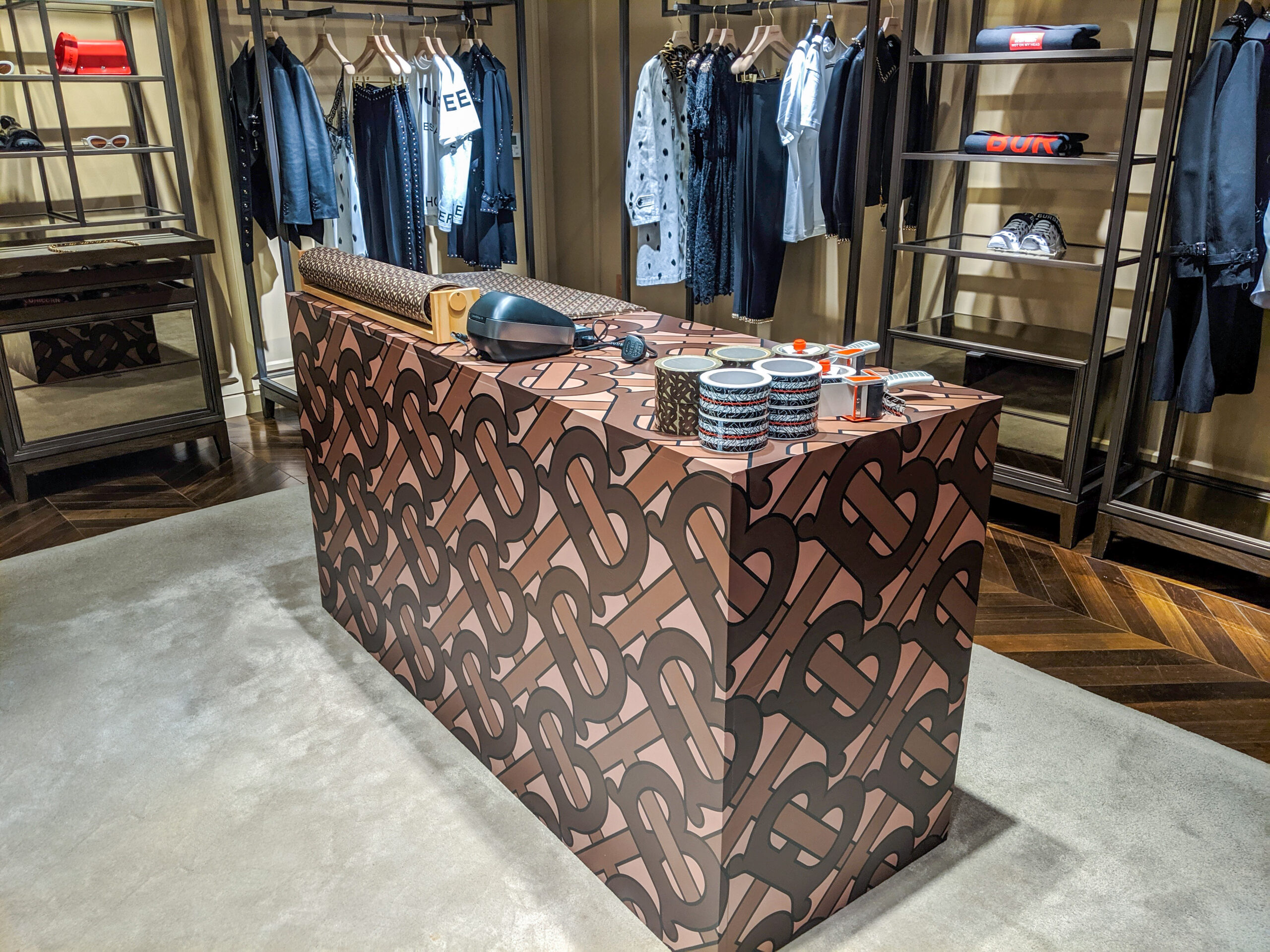 Burberry monogram-wrapped checkout counter display inside a Burberry retail store on 57th Street, with clothing racks visible in the background