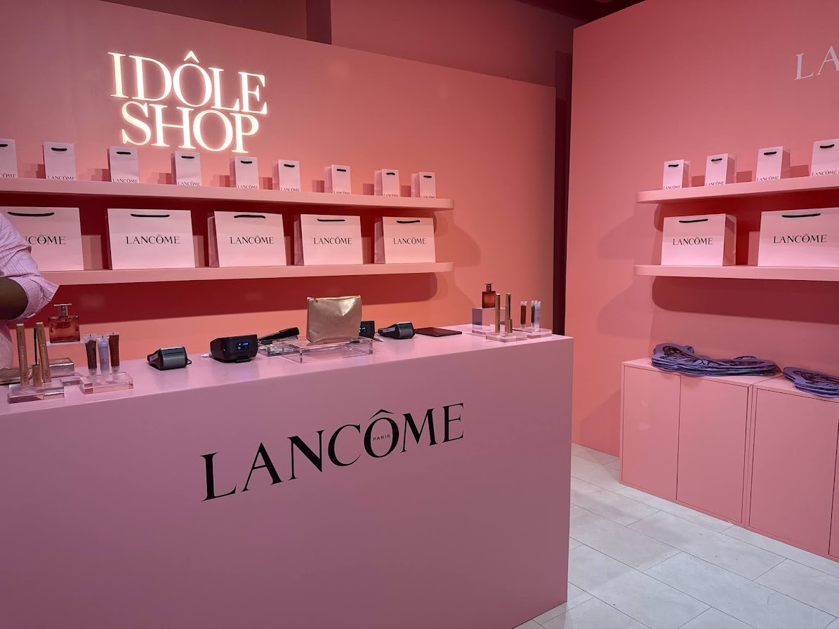 Lancôme Idôle Shop branded retail display with pink shelving, gift bags, and beauty products arranged on a counter inside a pop-up shop