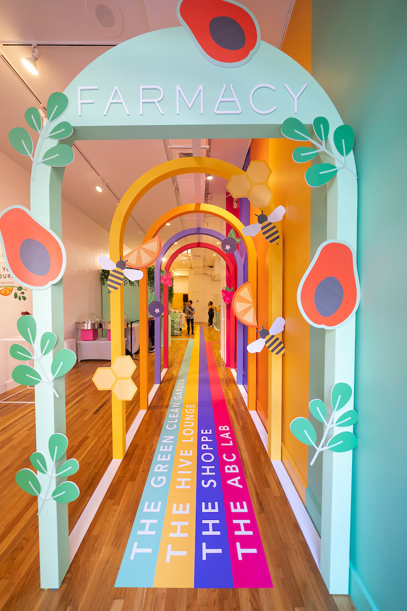 Colorful Farmacy Beauty branded hallway installation with layered archways, floor graphics, and illustrated avocado and bee decorations leading to The Green Clean Bar, Hive Lounge, The Shoppe, and ABC Lab