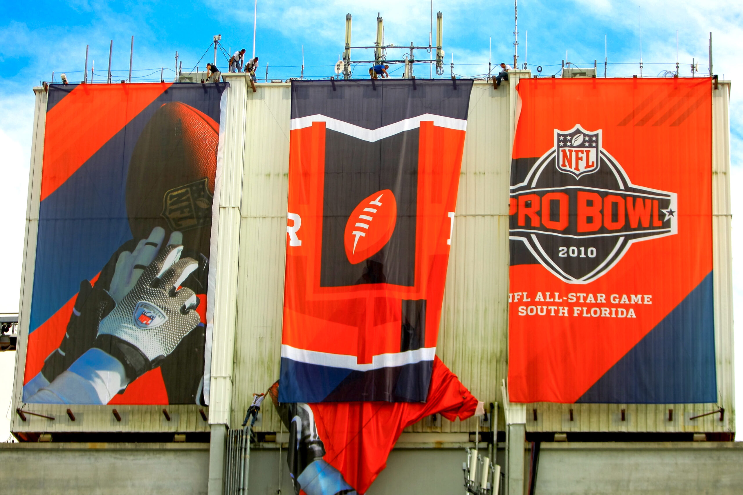 Large-scale NFL Pro Bowl 2010 banner installation being rigged on an outdoor structure in South Florida, featuring bold red and navy football graphics with the NFL All-Star Game logo