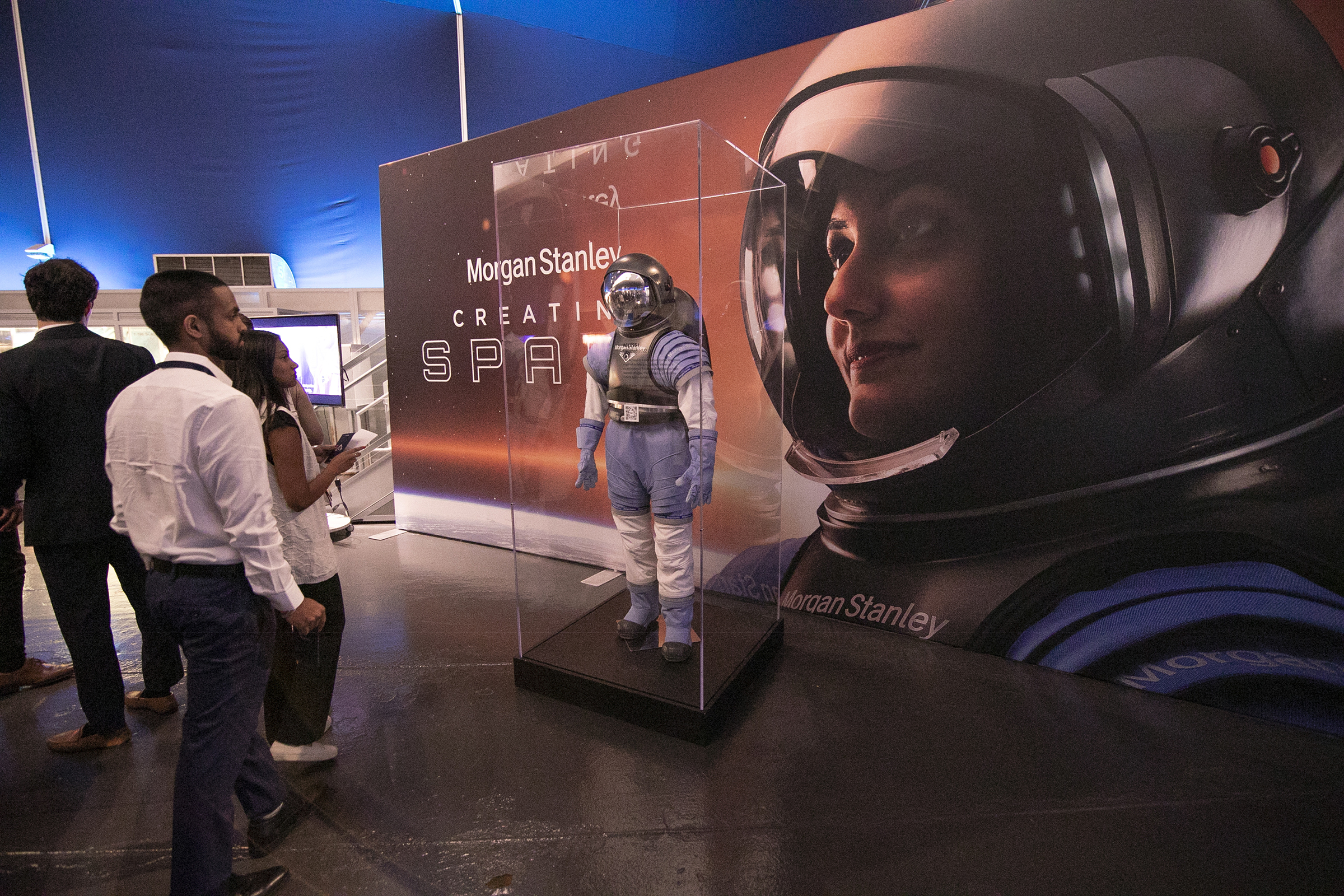 Attendees viewing a Morgan Stanley 'Creating Space' branded exhibit featuring a life-size astronaut suit display case and large-scale astronaut portrait backdrop at a corporate event