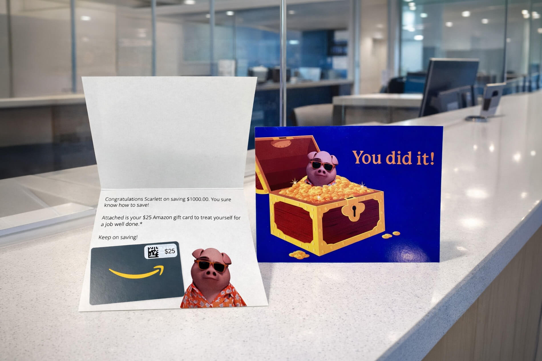 Avidia Bank direct mail package displayed on a bank counter, featuring a 'You did it!' savings congratulations mailer with treasure chest graphic, personalized letter, and Amazon gift card reward