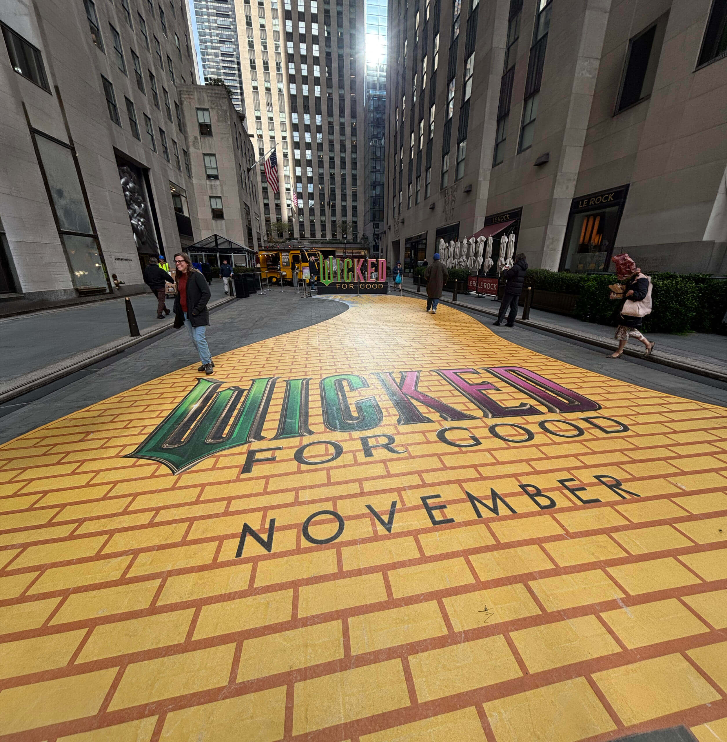 Large-scale Wicked: For Good yellow brick road floor graphic installation at Rockefeller Plaza NBC Store in New York City, with pedestrians walking on the branded pavement design