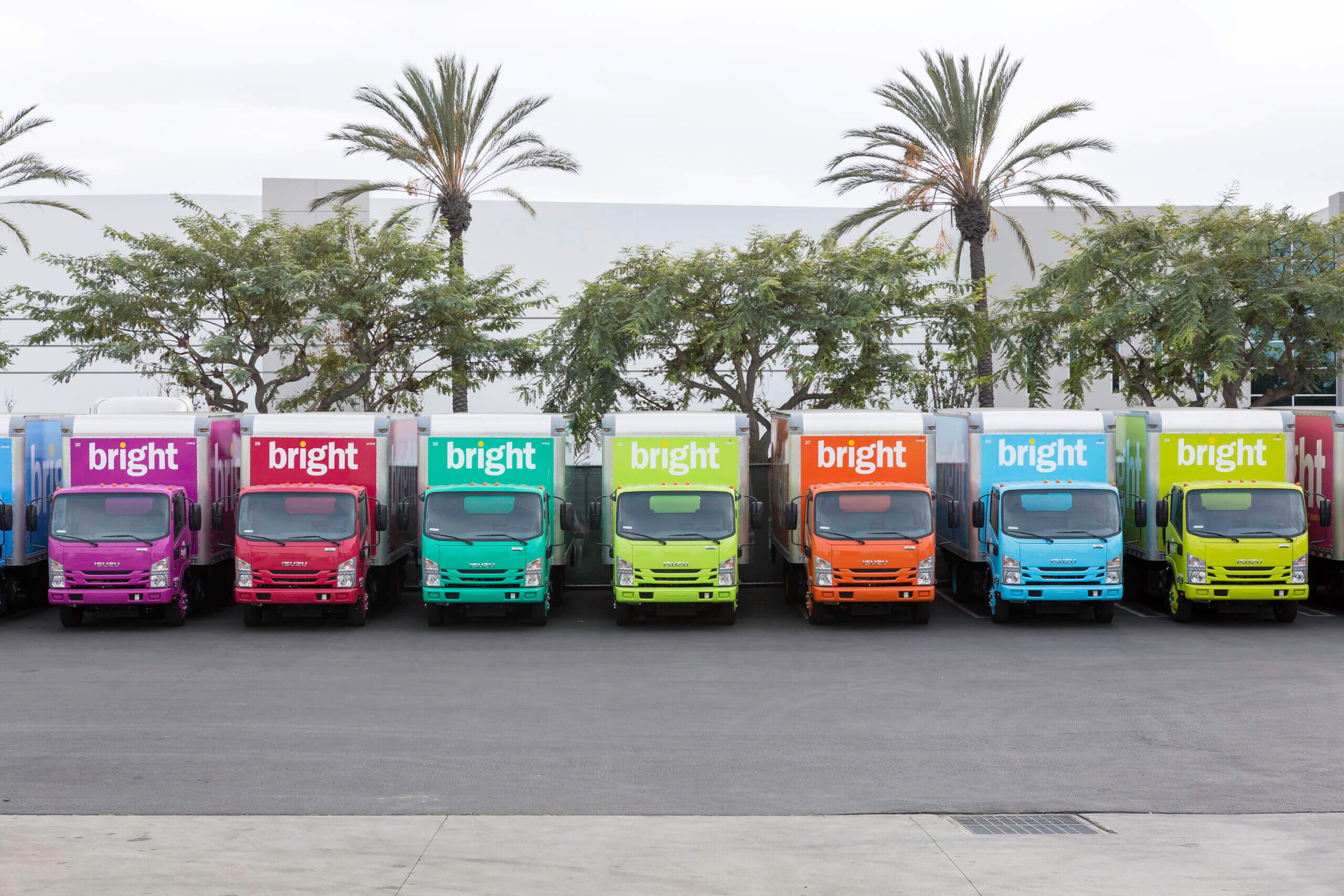 Fleet of eight Bright Event Rentals trucks wrapped in vibrant multicolor vehicle wraps — pink, teal, green, red, and yellow — lined up at the Los Angeles grand opening