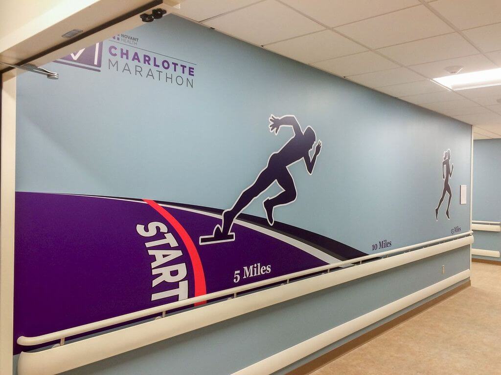 Charlotte Marathon branded wall mural in a healthcare facility hallway featuring a large runner silhouette graphic, race distance markers, and a purple start line design