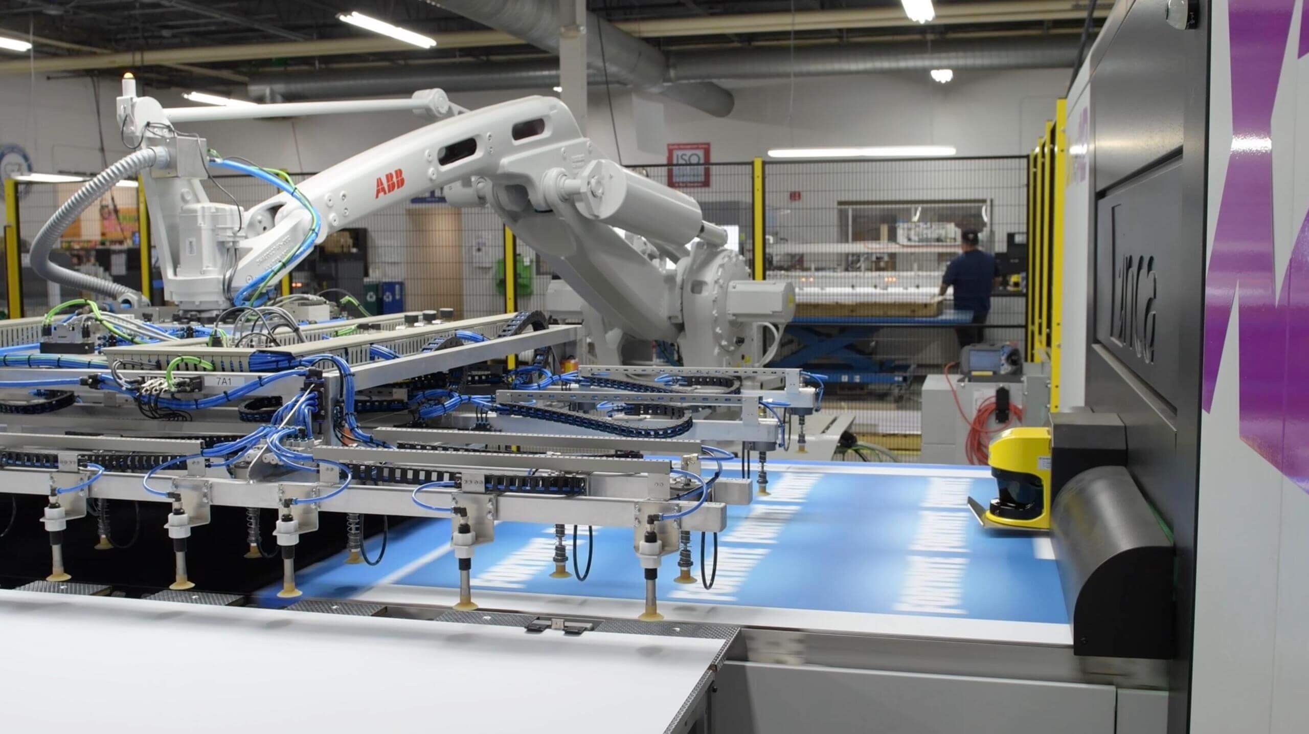 Vomela print production facility featuring an ABB robotic arm and automated large-format printing equipment on the production floor, with a worker visible in the background