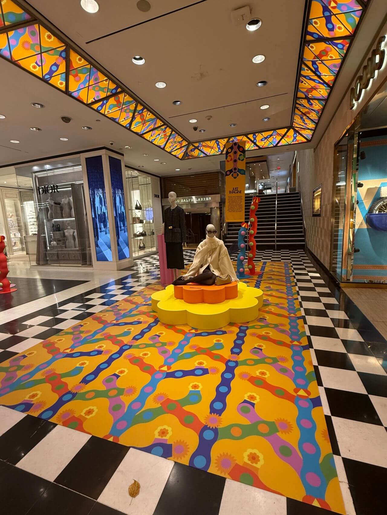 Bloomingdale's Yinka Ilori art installation featuring a vibrant multicolor patterned floor graphic, matching ceiling panels, and sculptural displays throughout the retail store atrium