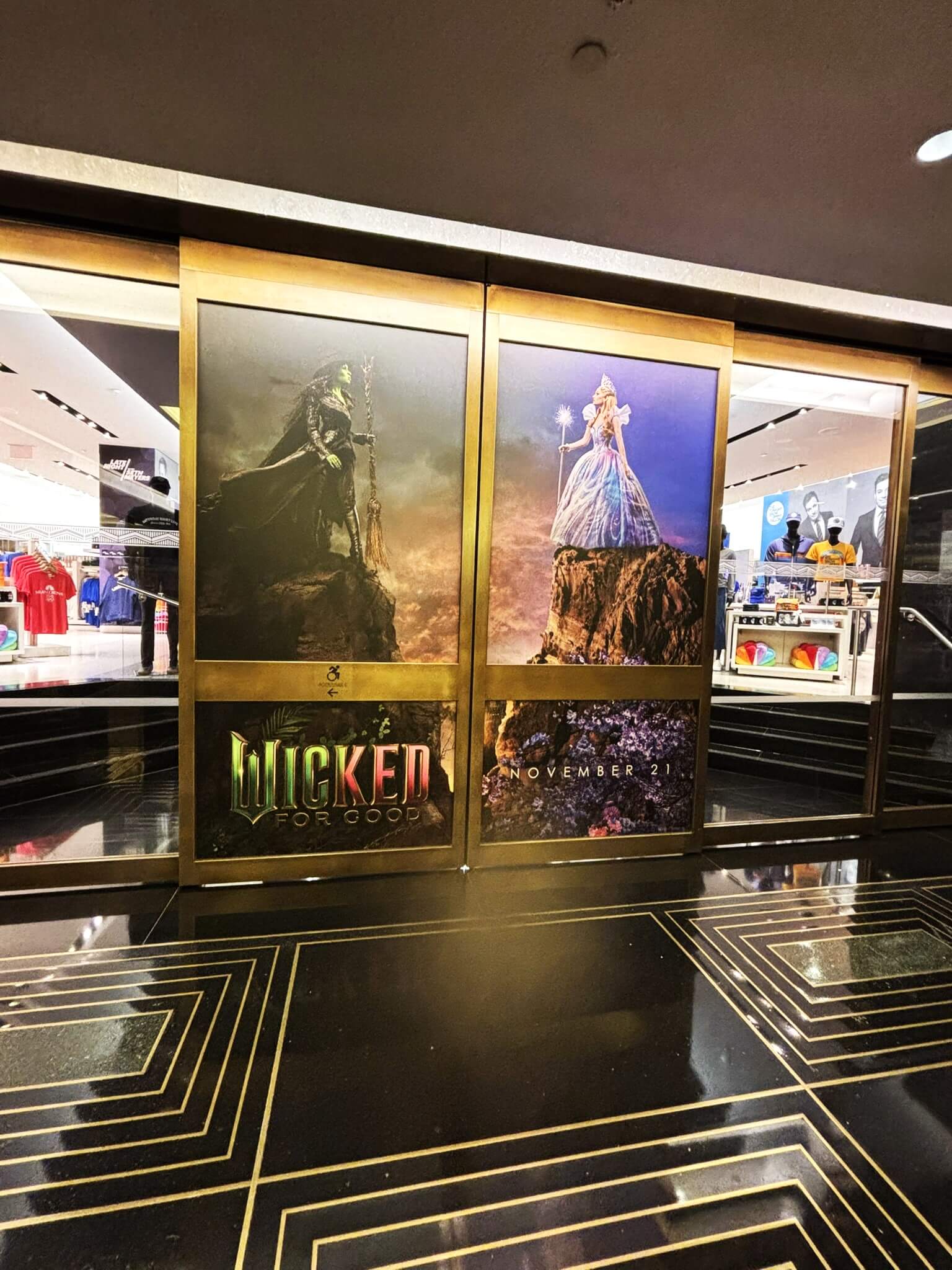 Wicked: For Good promotional door and window graphics installed on the front entrance of the NBC Store at Rockefeller Plaza, featuring Elphaba and Glinda character panels with November release date signage